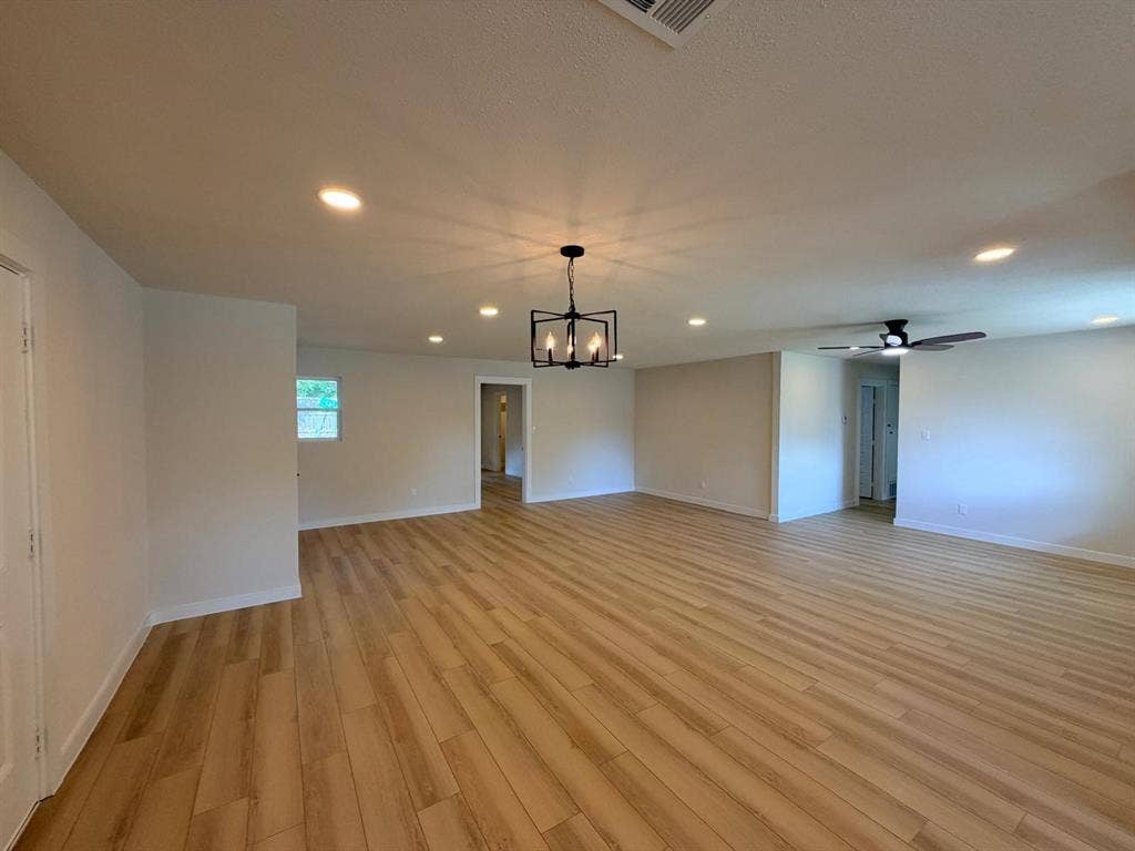Open interior space featuring wood-finish flooring, recessed lighting, a modern geometric chandelier, and a ceiling fan with integrated lighting