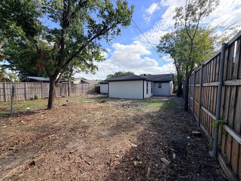 Rear yard featuring vertical siding exterior, wood privacy fencing, and mature trees
