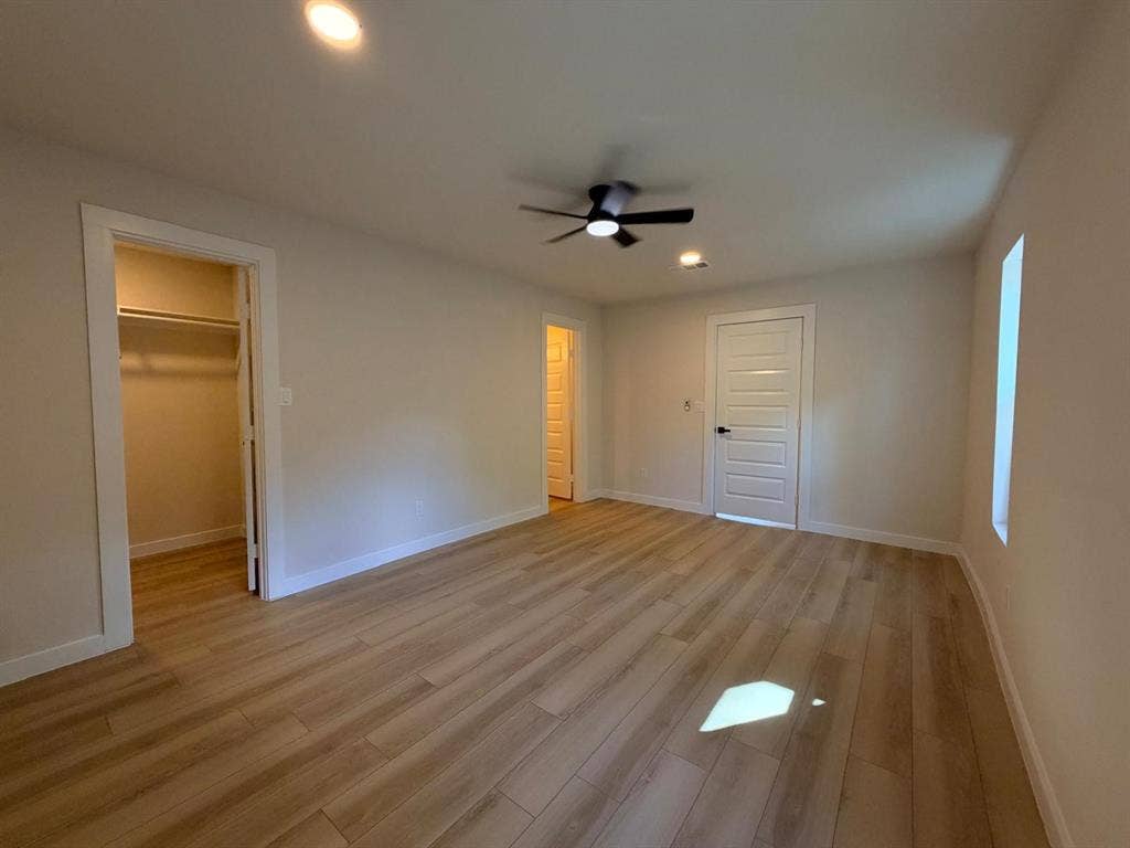 Neutral-toned room featuring wood-finish flooring, a multi-panel interior door, recessed lighting, and a ceiling fan with integrated light