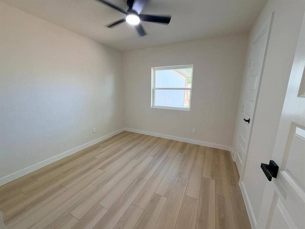Interior room featuring wood-finish flooring, a matte black ceiling fan with integrated lighting, a single-hung window, and a paneled door with matte black hardware