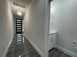Entry hallway featuring wood-finish flooring, a contemporary crystal-accented chandelier, and a modern six-panel door with glass inserts, accompanied by a powder room containing a white built-in vanity with a square sink