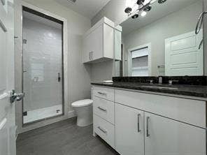 Bathroom featuring a walk-in shower with glass enclosure, white cabinetry, dark stone-finish countertop, and multi-bulb vanity lighting