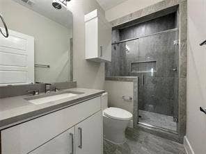 Bathroom featuring a white cabinet vanity with a composite countertop, an undermount sink, a walk-in shower with stone-finish tile surround, a glass sliding door, and a built-in shower niche