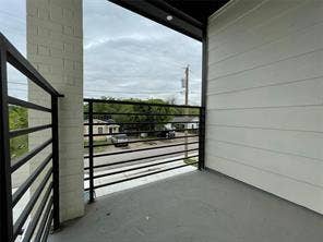 Covered balcony featuring horizontal metal railings, white horizontal siding, painted brick pillar, and solid flooring