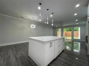 Kitchen island featuring a white stone-surface countertop, white cabinetry with silver-tone hardware, recessed ceiling lighting, three suspended pendant lights, and wood-finish flooring