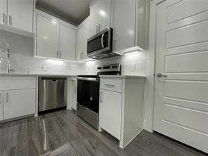 Kitchen featuring white cabinetry, stainless steel appliances, wood-finish flooring, and a subway tile backsplash