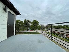 Elevated deck featuring horizontal black metal railings, a solid-surface floor, a black entry door, and wall-mounted exterior lighting