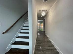 Staircase featuring dark-stained wood treads and white risers with a matching handrail, complemented by grey wood-finish flooring, a modern multi-light chandelier, and glass-paneled entry door