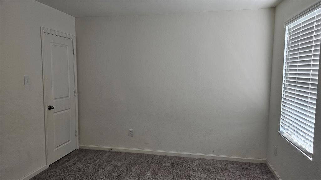 Neutral-toned wall-to-wall carpeting, white interior door, and window featuring horizontal slat blinds