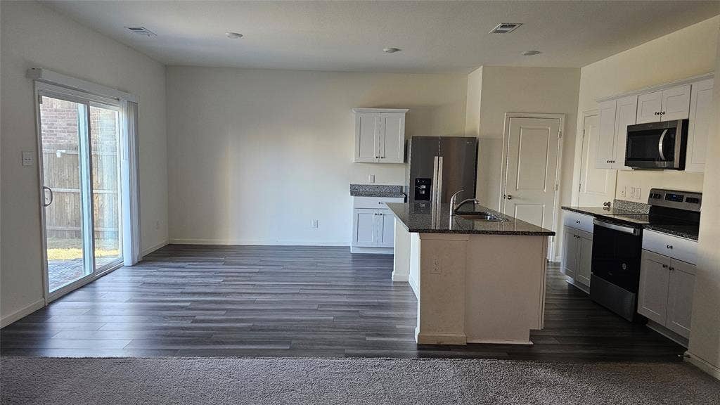 Kitchen featuring white cabinetry, stone-finish countertops, stainless steel appliances, a center island with an integrated sink, and wood-finish flooring