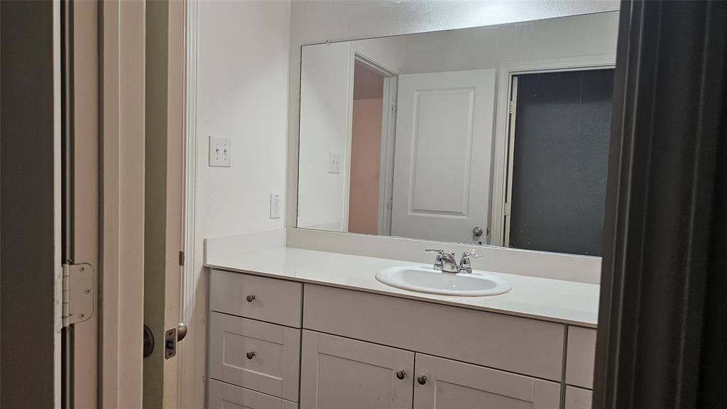 Bathroom vanity featuring a solid surface countertop, integrated oval sink, chrome dual-handle faucet, white Shaker-style cabinetry, and a large wall-mounted mirror