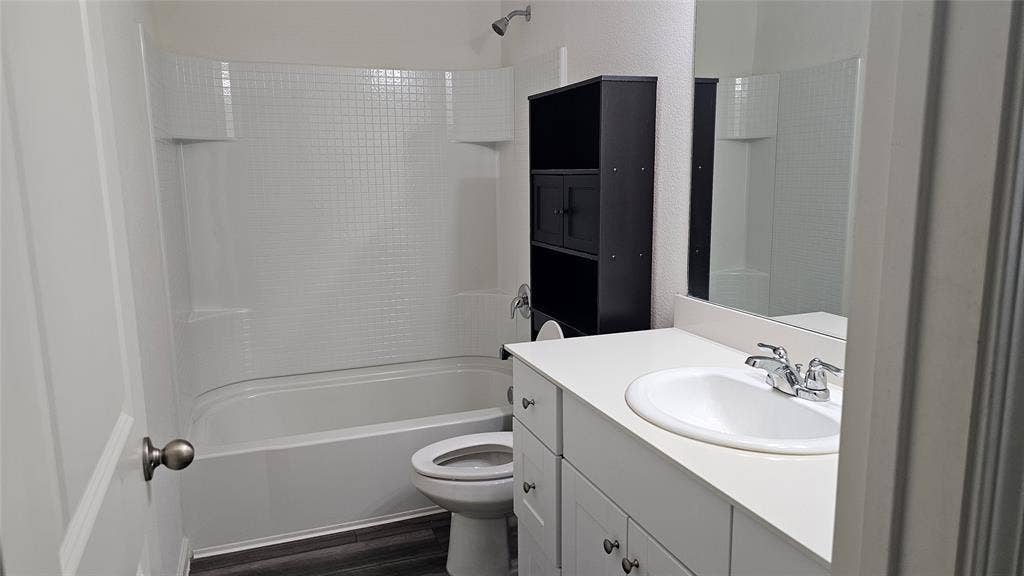 Bathroom featuring a tub-shower combination with tiled surround, vanity with an integrated basin, chrome-finish faucet, and wood-finish flooring