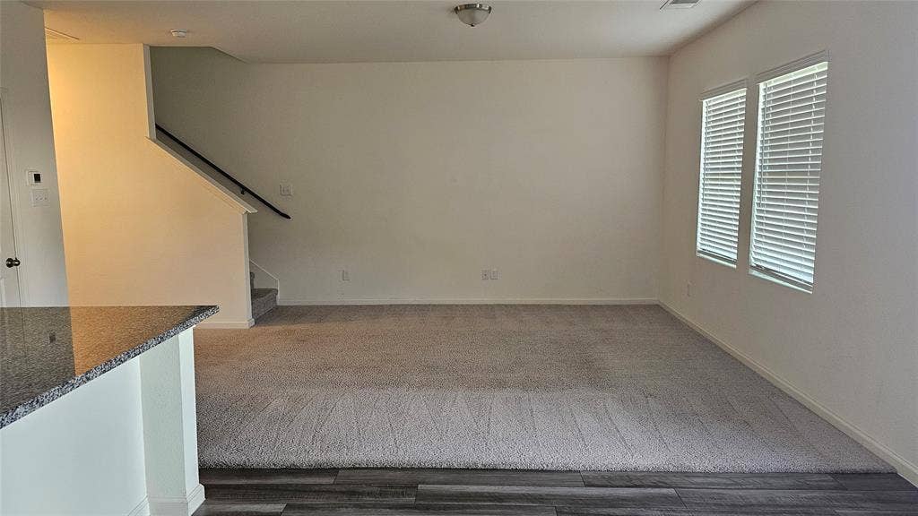 Interior area featuring carpeting, wood-finish flooring, a stairway with a black railing, and windows with horizontal blinds