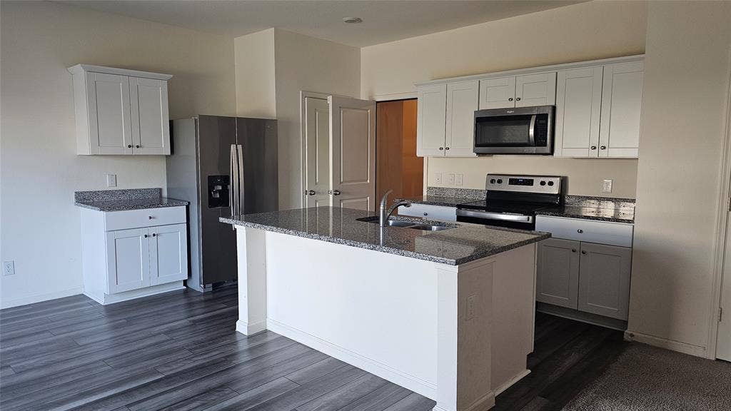 Kitchen featuring a central island with a stone-finish countertop, white cabinetry, stainless steel appliances, and wood-finish flooring