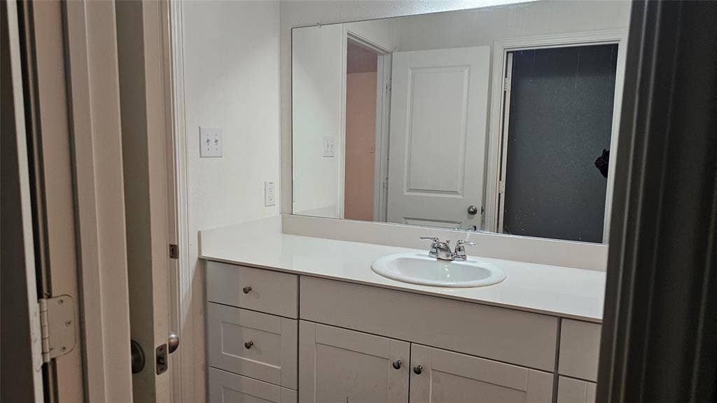 White vanity featuring a solid-surface countertop, integrated oval basin, polished chrome faucet, and expansive wall-mounted mirror