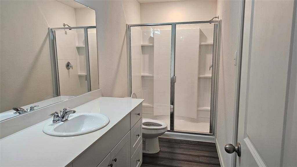 Bathroom featuring a white vanity with an integrated sink, a full-width mirror, wood-finish flooring, and a walk-in shower with a glass enclosure and built-in shelving