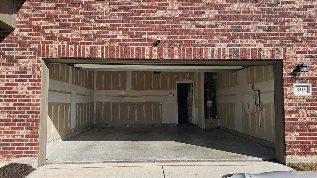 Attached two-car garage featuring red brick exterior, concrete flooring, and an integrated water heater