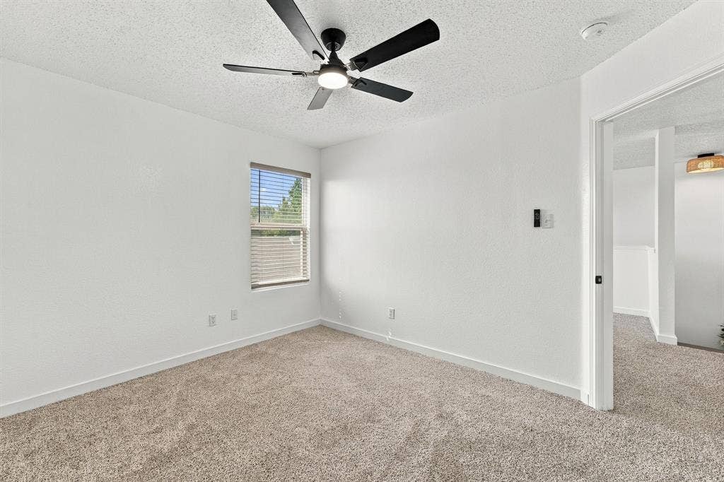 Room featuring neutral-toned carpeting, matte black ceiling fan with integrated lighting, and a single window with horizontal blinds