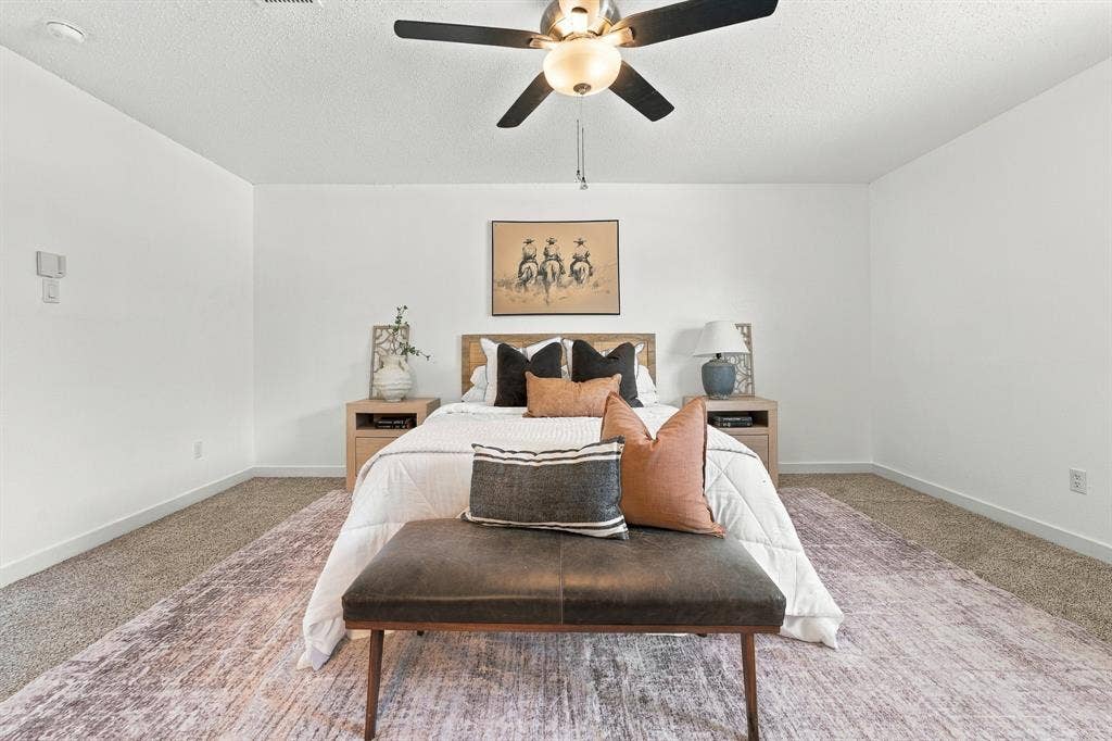 Neutral-toned carpeted flooring, textured ceiling, and centrally-mounted multi-blade ceiling fan with integrated lighting
