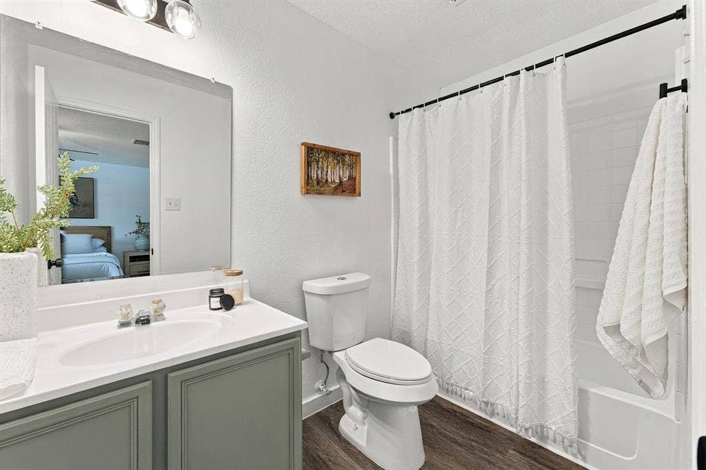Bathroom featuring a vanity with a solid surface countertop, an integrated sink, a large wall-mounted mirror, wood-finish flooring, and a shower-tub combination with a wall surround