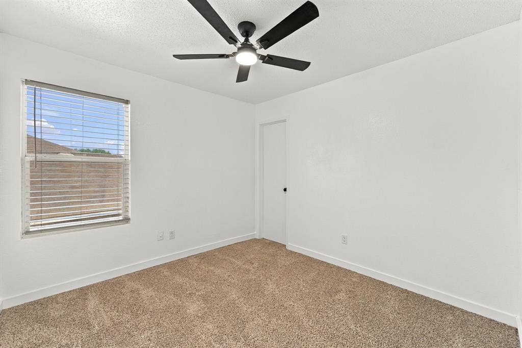 Neutral interior featuring carpeting, a multi-blade ceiling fan with integrated lighting, and a single-pane window with horizontal blinds