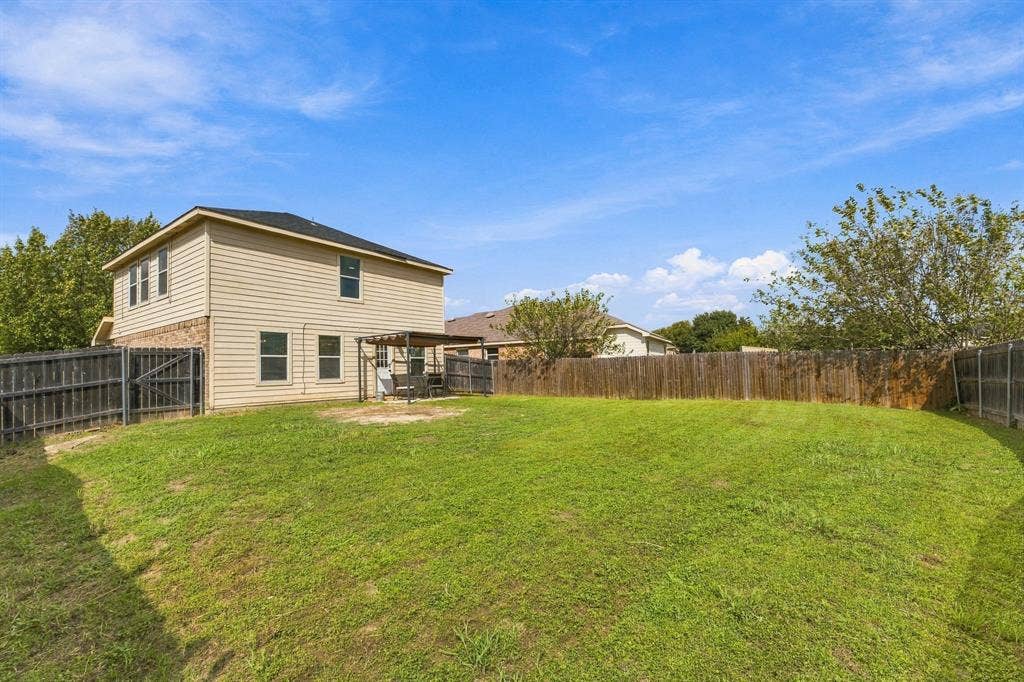 Expansive backyard featuring a sodded lawn, wood privacy fencing, and a pergola-covered patio