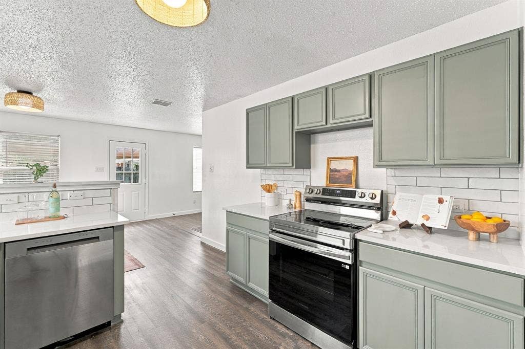 Kitchen featuring sage green shaker-style cabinetry, white quartz countertops, subway tile backsplash, stainless steel appliances, and wood-finish flooring