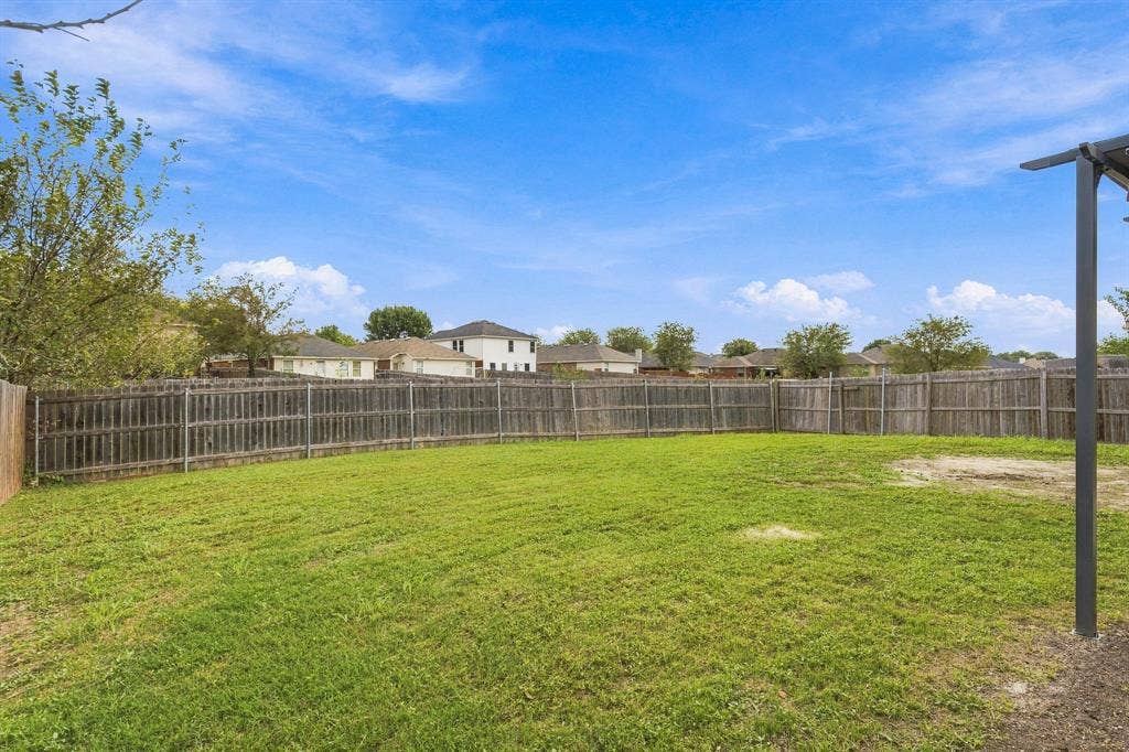 Expansive backyard featuring a level grass lawn, perimeter wood privacy fencing, and a partial metal patio cover support