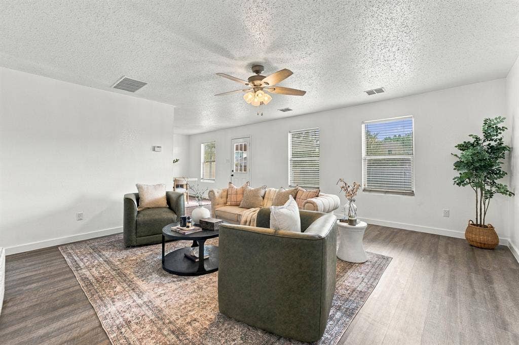 Open living area featuring wood-finish flooring, neutral walls, natural light through multiple windows, and a ceiling fan with integrated lighting