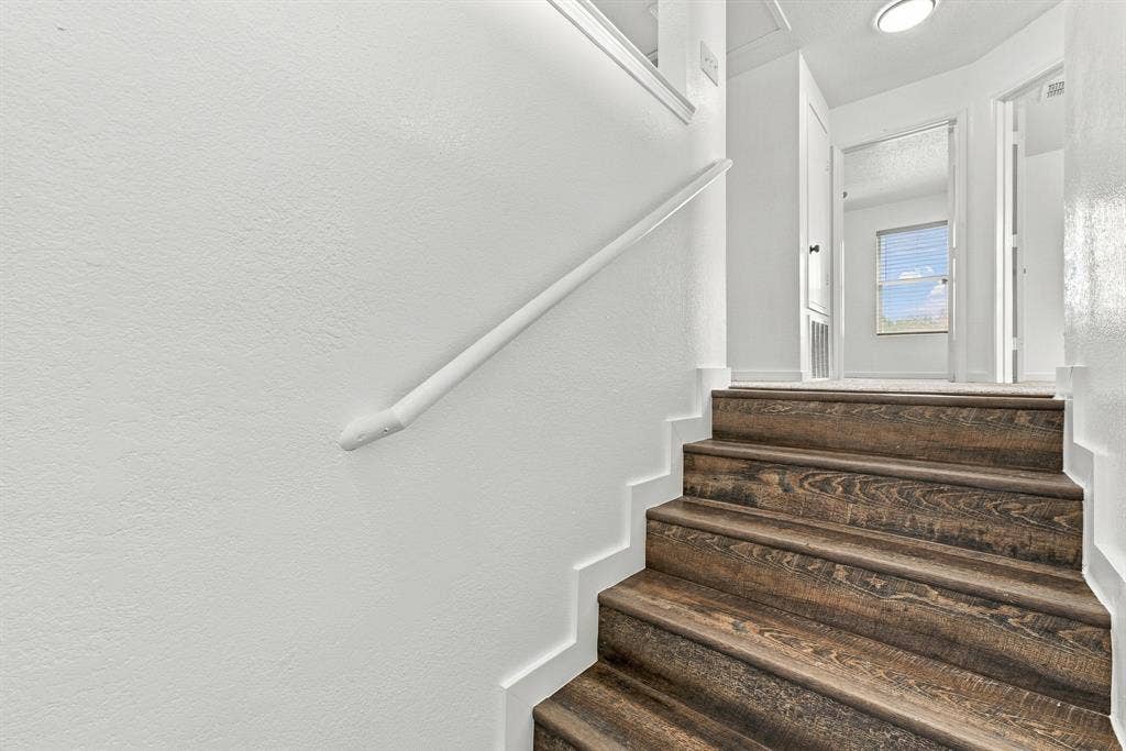 Staircase featuring wood-finish treads, white painted walls, and a matching handrail
