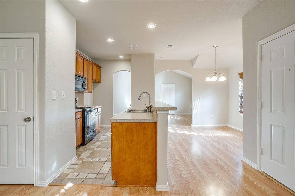 Kitchen featuring wood cabinetry, stone-finish countertops, ceramic tile flooring, and integrated lighting, including a multi-light chandelier