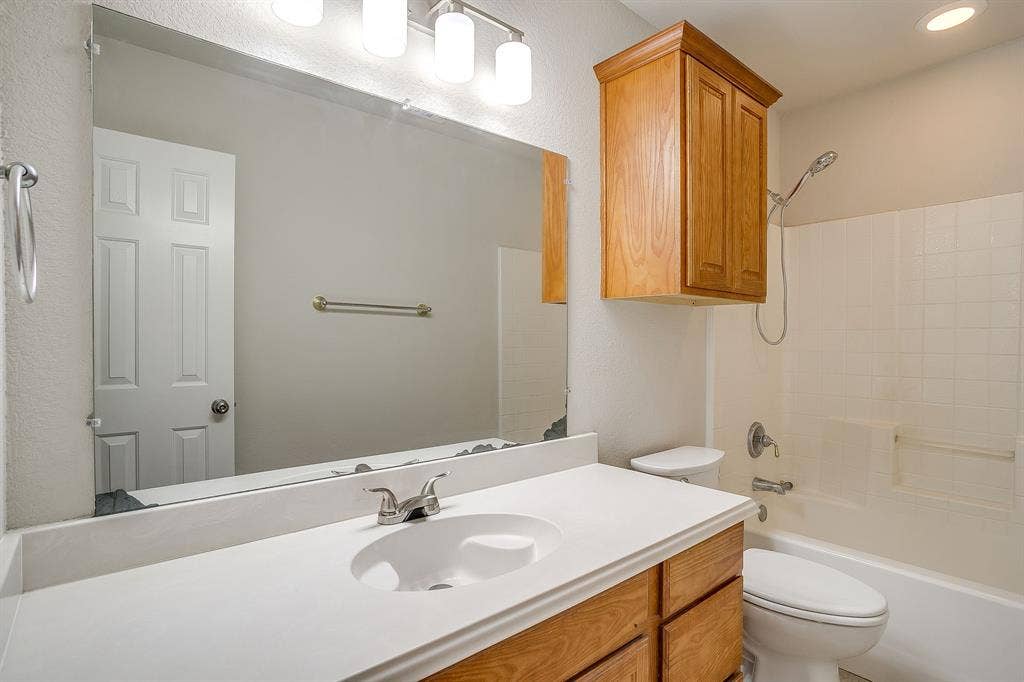 Bathroom vanity featuring a solid-surface countertop with an integrated basin, wood-finish cabinetry, wall-mounted storage cabinet, full-width mirror, and four-light overhead fixture