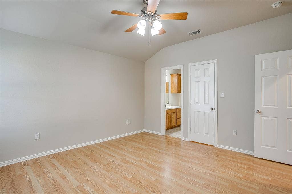 Vaulted ceiling featuring a ceiling fan with integrated lighting, wood-finish flooring, and six-panel interior doors
