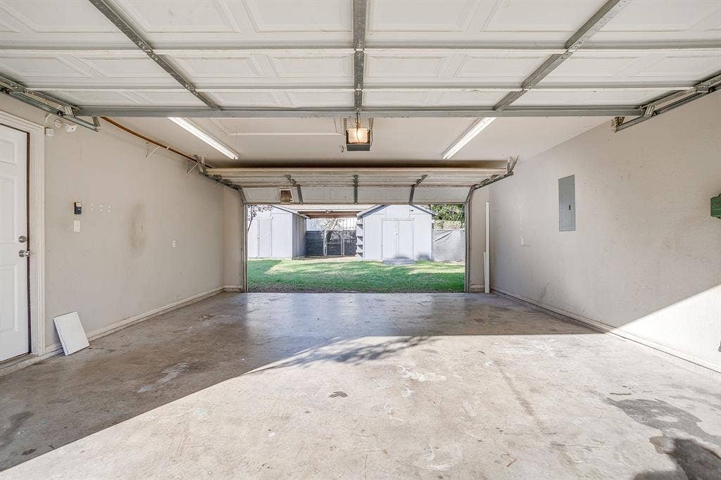 Multi-car garage featuring a concrete floor, overhead lighting, an integrated electrical panel, and a direct-entry door, with an open portal to an exterior grass yard