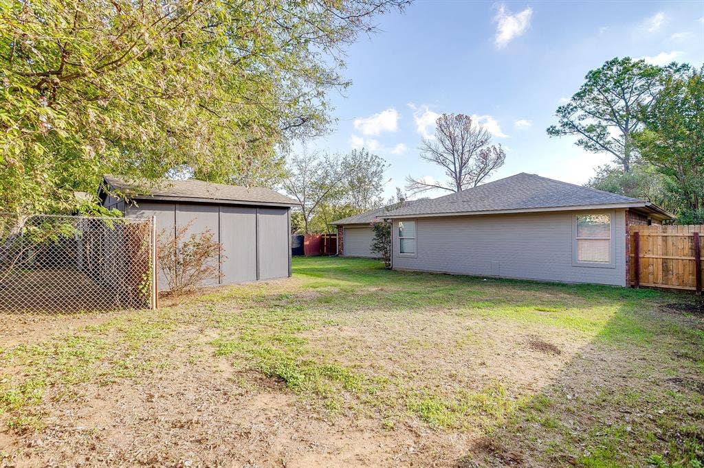 Expansive backyard featuring mature trees, a detached storage structure, chain-link fencing, and wood privacy fencing