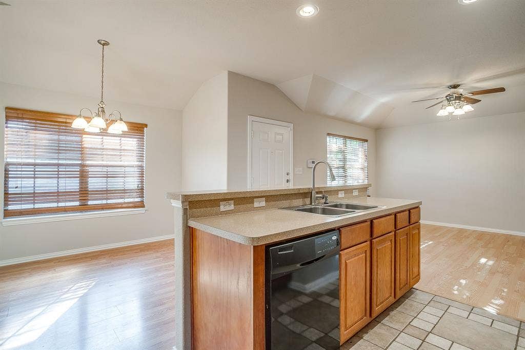 Kitchen island featuring wood cabinetry, a dual-basin stainless steel sink with a goose-neck faucet, and a dishwasher