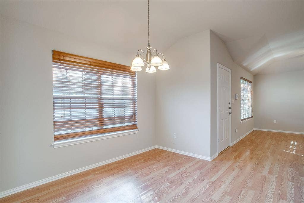Interior space featuring wood-finish flooring, vaulted ceilings, multi-light chandelier, and large windows with horizontal blinds