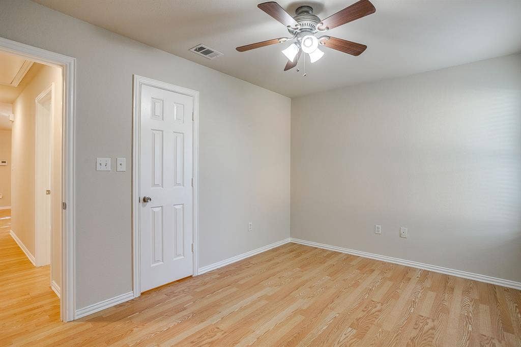 Room featuring wood-finish flooring, a neutral wall color palette, a six-panel interior door, and a ceiling fan with integrated lighting
