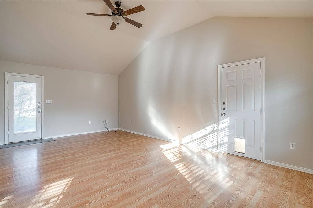 Vaulted ceiling featuring a central wood-finish ceiling fan, wood-finish flooring, and two exterior doors with glass inserts