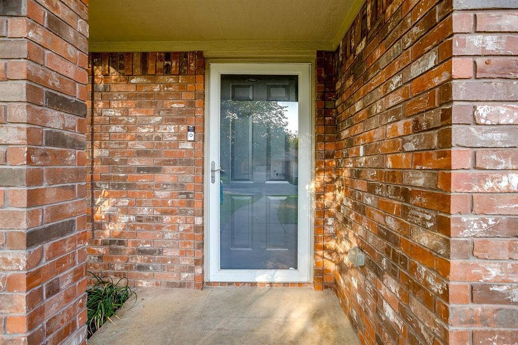 Exterior entryway featuring multi-toned masonry brickwork, a recessed porch, and a white-framed glass storm door