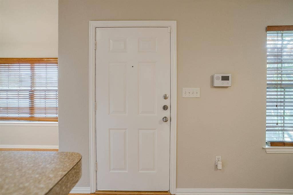 Six-panel entry door with integrated peephole, wall-mounted digital thermostat, and windows featuring horizontal blinds