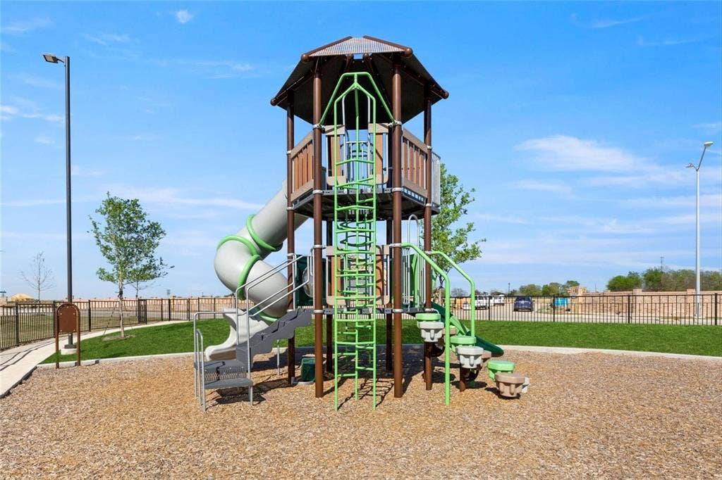 2808 Spring Side Drive, Royse City, TX 75189 Multi-level playground structure featuring a spiral slide, vertical climbing ladder, and integrated stairs, set within a manicured area with wood-chip ground cover and perimeter metal fencing