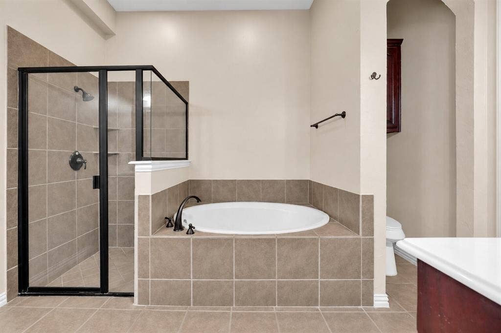 Built-in soaking tub with a tile surround, glass-enclosed shower with matte black fixtures, and tile flooring