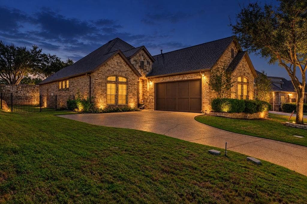 Stone-veneer exterior featuring a multi-gabled roofline, multi-panel garage door, arched windows, and manicured landscaping