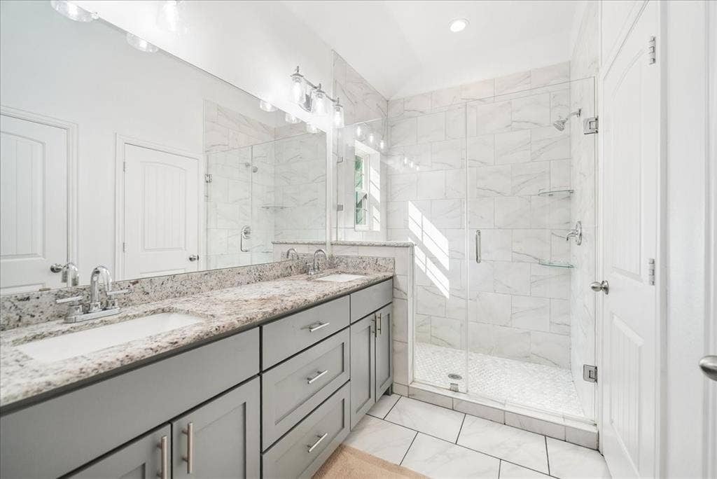 7320 County Road 3512, Quinlan, TX 75474 Bathroom featuring a grey dual-sink vanity with a stone countertop, a glass-enclosed shower with tiled walls and flooring, and full-width vanity mirror with integrated lighting