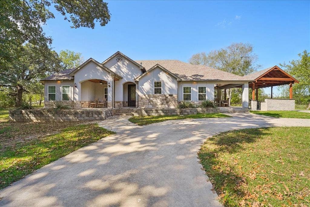 7320 County Road 3512, Quinlan, TX 75474 Single-story residence with a stone and stucco facade, concrete driveway, covered porch, and attached outdoor living structure with a stone-finish built-in counter