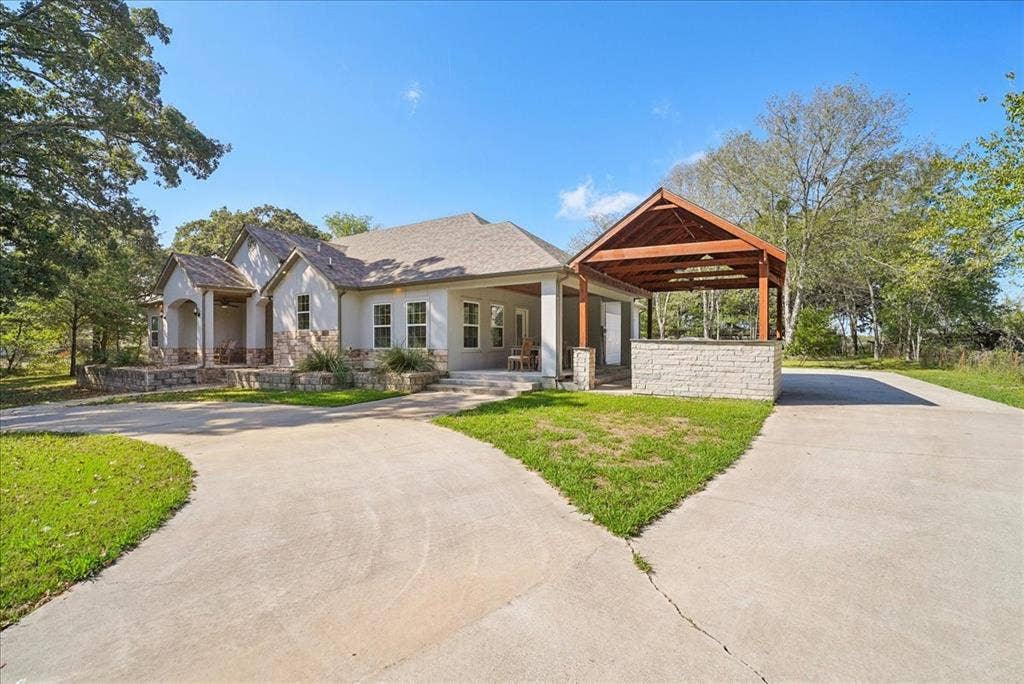 7320 County Road 3512, Quinlan, TX 75474 Exterior featuring masonry cladding, a concrete driveway, a covered patio, and a detached open-air pavilion with a stone-finished base