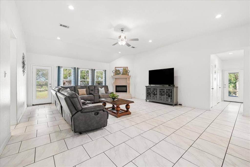 7320 County Road 3512, Quinlan, TX 75474 Vaulted ceilings, large-format tile flooring, a corner fireplace with a decorative mantel, multiple windows with natural light, and recessed lighting
