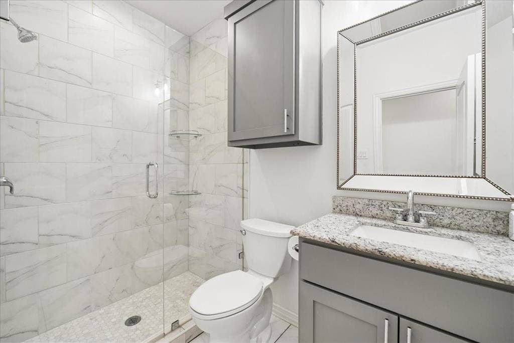 7320 County Road 3512, Quinlan, TX 75474 Walk-in shower with floor-to-ceiling tile, grey shaker-style vanity, stone-finish countertop, under-mount sink, and wall-mounted storage cabinet