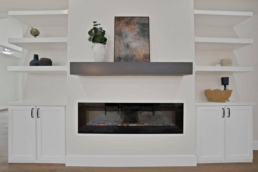 Linear electric fireplace featuring a dark surround, complemented by built-in lower cabinetry with matte black hardware and white floating shelving
